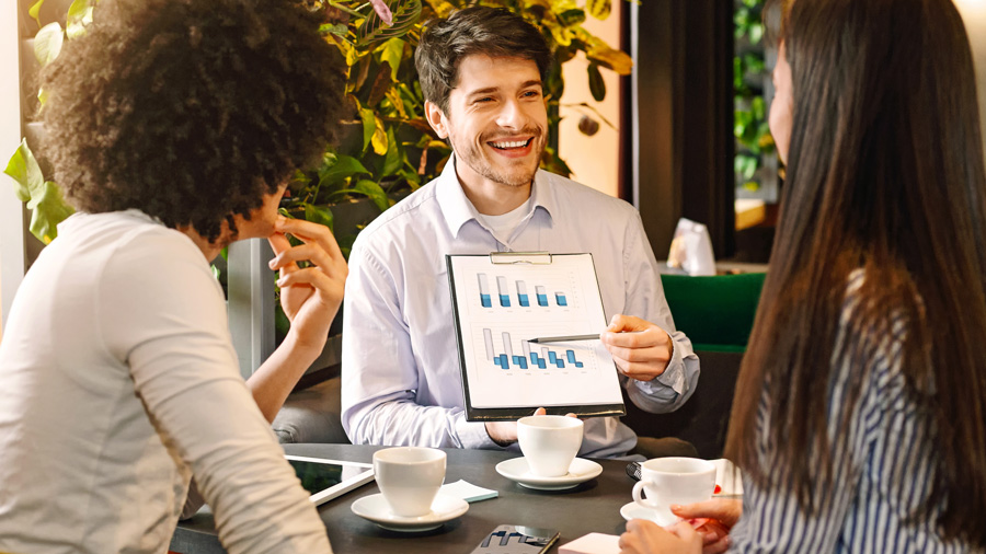 Un expert-comptable présente une analyse de rentabilité à deux entrepreneuses lors d’un rendez-vous professionnel, en expliquant un graphique sur l’évolution des ventes.