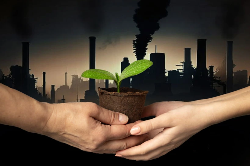 Deux personnes se transmettent une jeune pousse verte devant une usine en activité, illustrant la transition écologique de l’entreprise